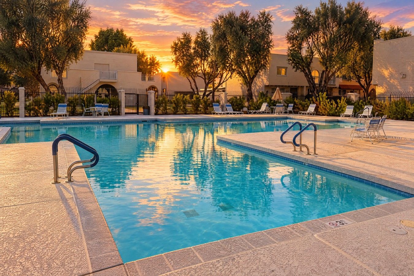 En pool med solstolar och en solnedgång i bakgrunden.
