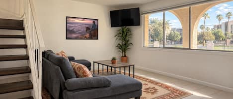 Living room: large sectional, smart TV and a wide window framed by stucco arches