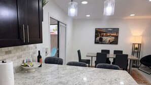Una cocina con armarios oscuros, encimera de mármol y comedor con mesa y sillas.