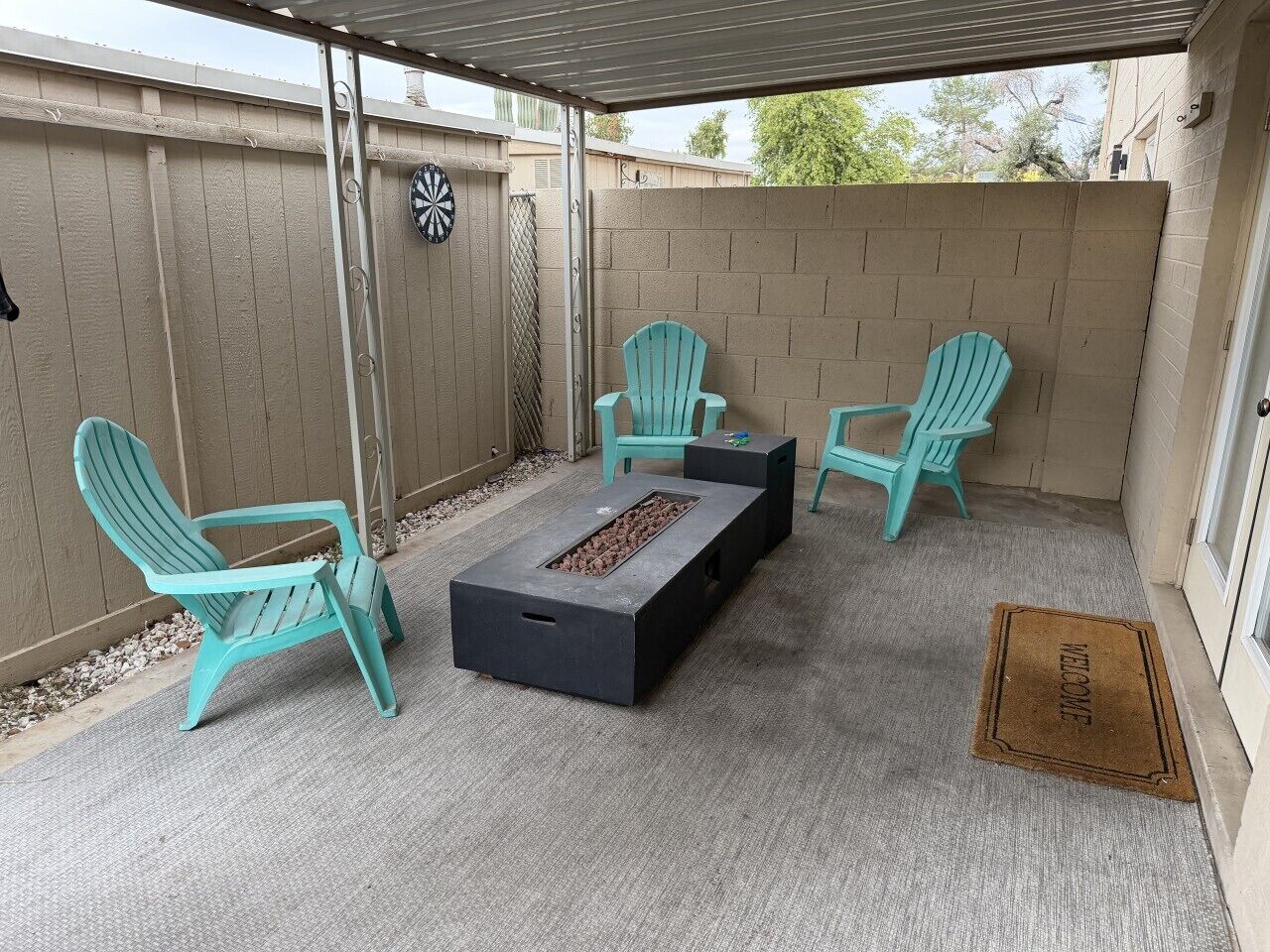 Un patio couvert avec un foyer, deux fauteuils Adirondack et un paillasson.
