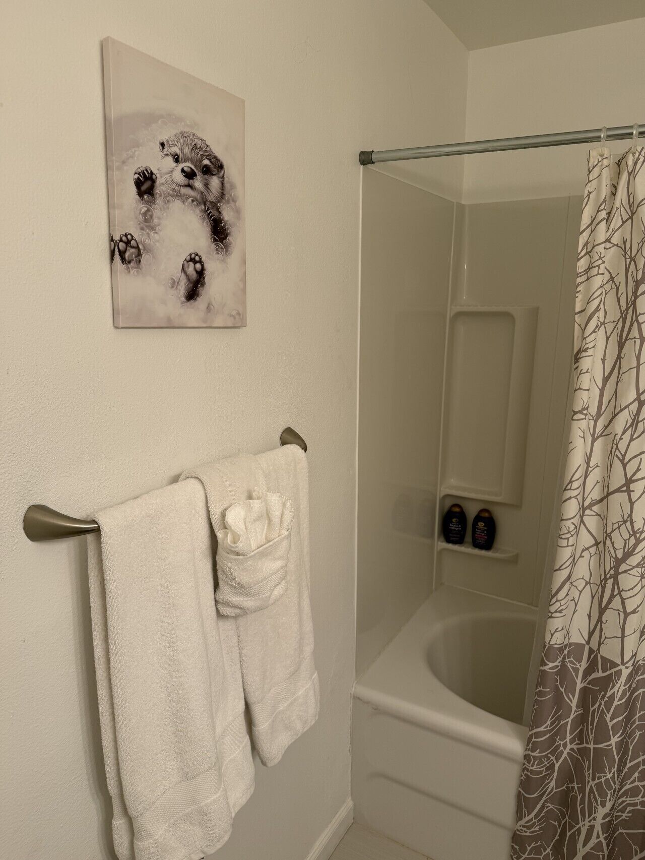 A bathroom with a bathtub, a towel rack with two towels, a shower curtain, and a wall-mounted artwork.