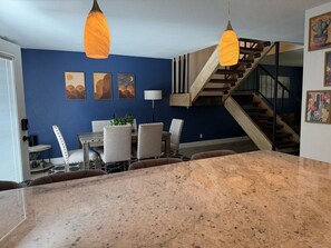 Eine Küche mit Granitarbeitsplatte, ein Essbereich mit Stühlen und einem Tisch sowie eine Treppe, die zu einer oberen Etage führt.