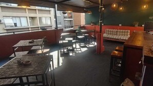 A restaurant with tables and chairs, a sofa, and hanging lights. - Mediterranea Hostel (Córdoba)