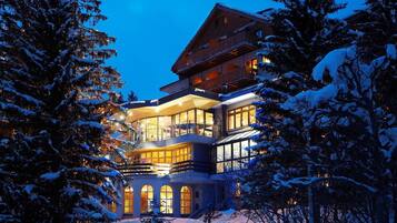 A multi-story building with large windows and balconies, surrounded by snow-covered trees.