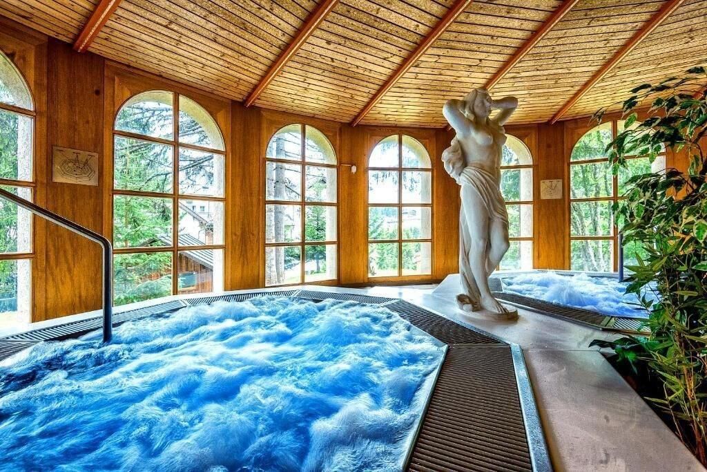 Ein Wellnessbereich mit Whirlpool, Holzwänden und großen Bogenfenstern.
