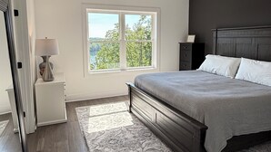 Ein Schlafzimmer mit einem Bett, Deckenventilator, Nachttisch, Lampe, Fenster mit Blick und einem gemusterten Teppich.
