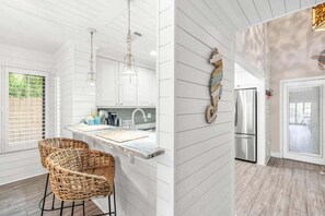 A modern kitchen with white cabinetry, a marble countertop, wicker chairs, and a stainless steel refrigerator. - 🦩Book Me Baby! Coastal Krewe in Miramar Beach🦩 (Miramar Beach)