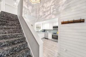 A modern kitchen with white cabinets, a wooden staircase, and a hanging light fixture. - 🦩Book Me Baby! Coastal Krewe in Miramar Beach🦩 (Miramar Beach)