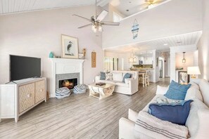 A spacious living room with a fireplace, a television, and a ceiling fan. - 🦩Book Me Baby! Coastal Krewe in Miramar Beach🦩 (Miramar Beach)