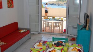 Ein Zimmer mit einem roten Sofa, einem Esstisch mit Frühstücksangebot und einem Balkon mit Meerblick.