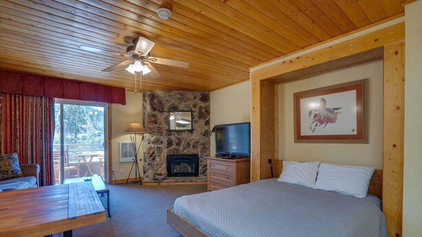Quarto com cama, televisão, lareira de pedra, ventoinha no teto e espaço de refeições com mesa e cadeiras.