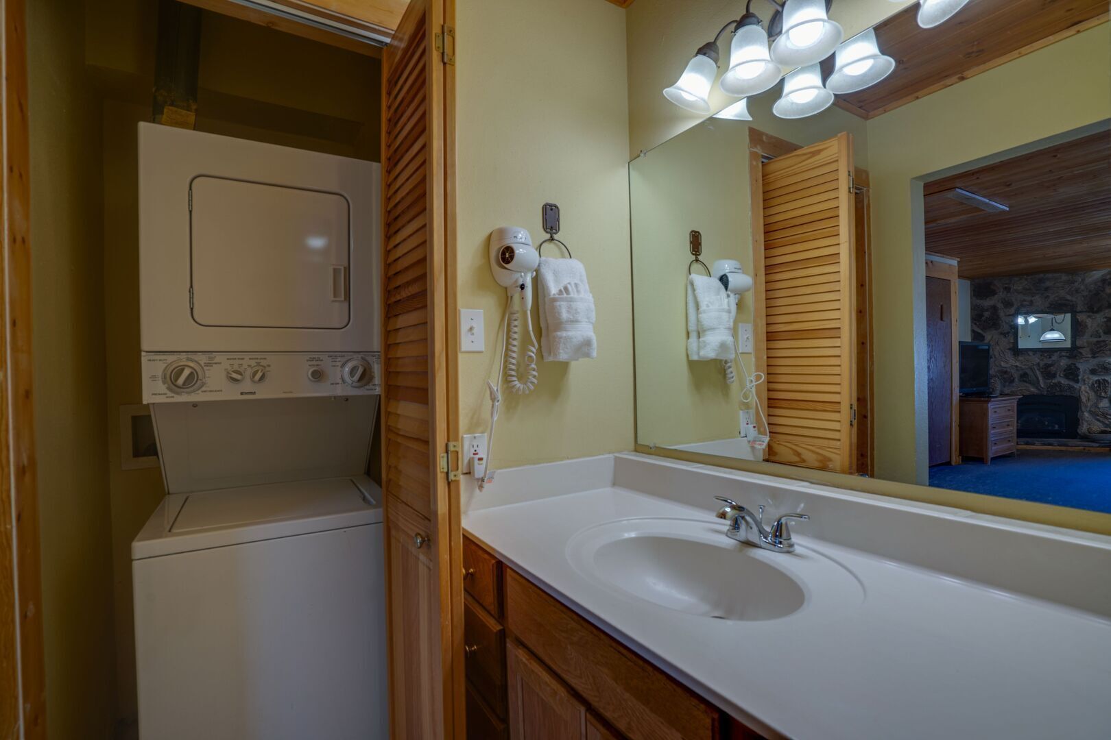 A compact bathroom with a built-in washer and dryer, a sink with a mirror, and a stone wall.