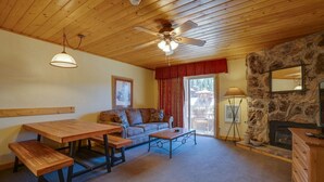 A cozy living room with a wooden ceiling, a stone fireplace, a sofa, a dining table, and a bench. - Suite at the Eagle Wing of the Lodge at Angel Fire Resort (Angel Fire)