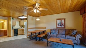 A living room with a sofa, a wooden coffee table, a dining table with benches, a ceiling fan, and a kitchen in the background. - Suite at the Eagle Wing of the Lodge at Angel Fire Resort (Angel Fire)