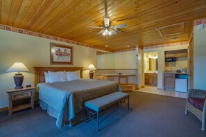 A bedroom with a bed, bedside tables, a bench, a ceiling fan, a bathroom with a sink and mirror, and a kitchenette with a microwave. - Suite at the Eagle Wing of the Lodge at Angel Fire Resort (Angel Fire)