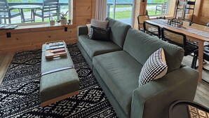Interior de uma cabana de madeira com sofá, puf, mesa de jantar e cadeiras.