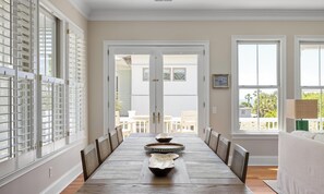 A dining room with a long table, chairs, and a view through a door to the outside. - Private Pool + Rooftop Ocean Views (Isle Of Palms)