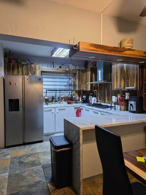 Een moderne keuken met een centraal eiland, roestvrijstalen apparatuur en een houten plafond.