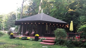 Een houten hut met een veranda, zitplaatsen buiten en lichtslingers.