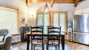 Een eetgedeelte met een houten tafel en stoelen, een kroonluchter, en een keuken met een koelkast.