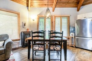 A dining area with a wooden table and chairs, a chandelier, and a kitchen with a refrigerator. - Welcome to our cottage🥰 (Tiny)