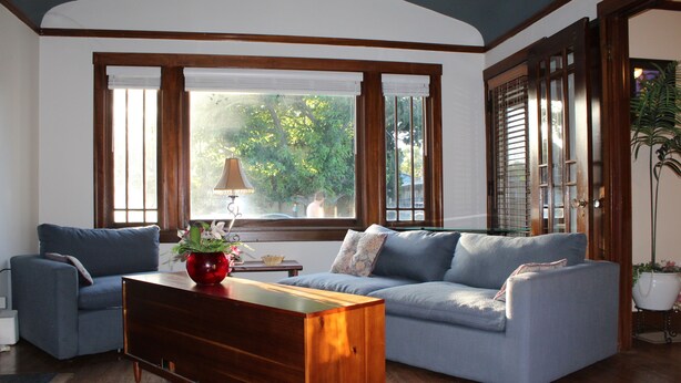 Ein Wohnzimmer mit blauem Sofa, Couchtisch aus Holz und einem Fenster mit Jalousien.
