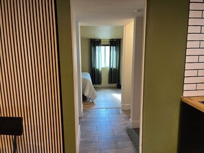 A hallway with a wooden slat wall, a bed with a white bedspread, and a window with dark curtains. - Cozy bungalow in Central Phoenix near stadiums, hospitals, & restaurants (Phoenix)