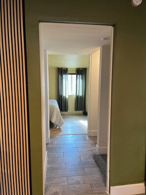 A hallway leading to a bedroom with a bed, a window with curtains, and a door. - Cozy bungalow in Central Phoenix near stadiums, hospitals, & restaurants (Phoenix)