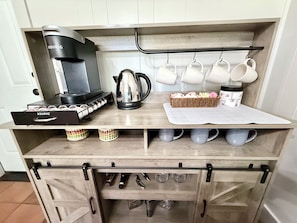 Eine Küchenzeile mit einer Keurig-Kaffeemaschine, einem Wasserkocher, einem Kaffeetassenhalter, einem Tablett mit Servietten und einer Schublade mit Besteck.