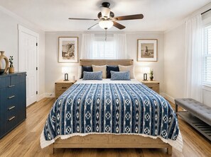 Ein Schlafzimmer mit einem Bett, Deckenventilator, Nachttischen, einer Bank und gerahmten Bildern an der Wand.