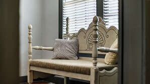 A wooden bench with a cushioned seat and backrest, positioned in a room with a patterned rug and a window with blinds. - The Downtown, Stay in the Heart of Mossy Creek (Jefferson City)