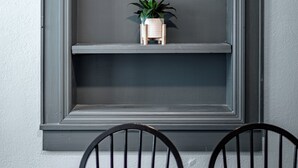 A dining area with a wooden table and chairs, a grey wall, and a shelf with a plant. - The Downtown, Stay in the Heart of Mossy Creek (Jefferson City)