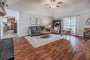 A living room with hardwood flooring, a ceiling fan, a sofa, a coffee table, and a bookshelf.