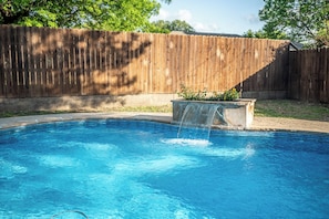 A backyard with a swimming pool, a wooden fence, and a planter with plants.