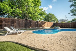 Un patio trasero con piscina, dos sillones de descanso y valla de madera.