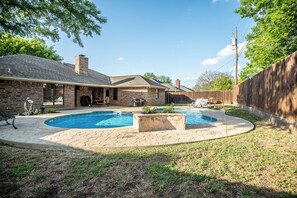 Un patio trasero con piscina, una casa de ladrillo y una valla de madera.