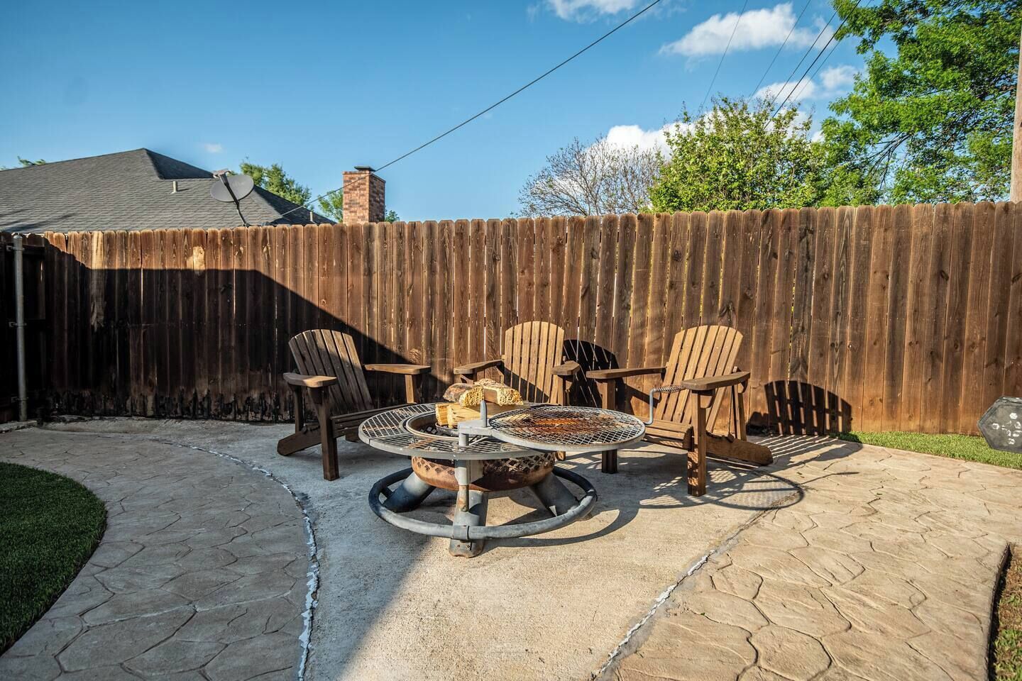 Un patio trasero con un pozo de fuego, cuatro sillas Adirondack y una valla de madera.