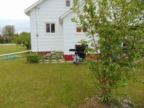A white house with a red trim, a small yard, and a tree in the foreground.