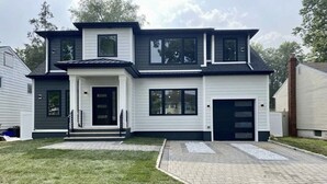 Uma casa moderna de dois andares, com garagem frontal, varanda coberta e entrada por um caminho de asfalto.