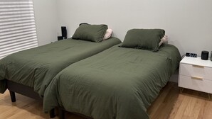 Quarto com duas camas, uma mesa de cabeceira branca e piso de madeira.