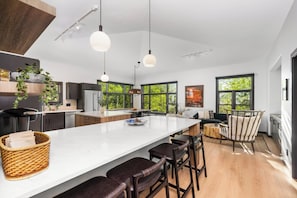 A modern kitchen with a large island, bar stools, and a view of greenery through large windows. - Luxury Remodeled 4BR Telluride Home | Hot Tub, Walk to Gondola & Main St | Sleeps 12 (Telluride)
