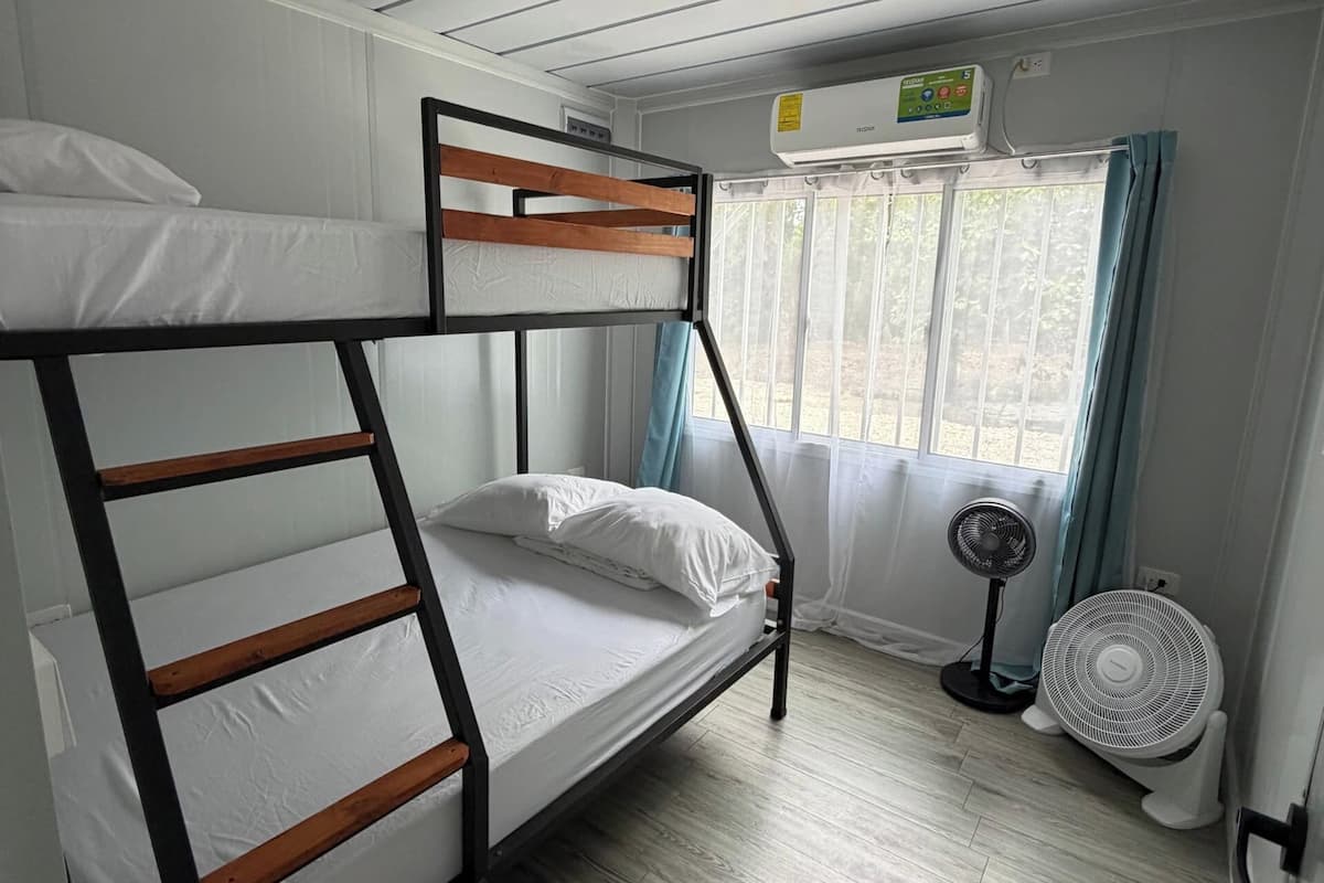 A bunk bed room with a ceiling fan, an air conditioning unit, and a window with curtains.