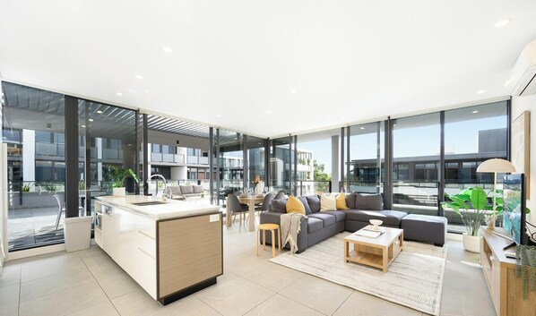 A modern interior with a kitchen, dining area, and living space with large windows. - KozyGuru | Parramatta | Sleek Skyline Retreat (Parramatta)