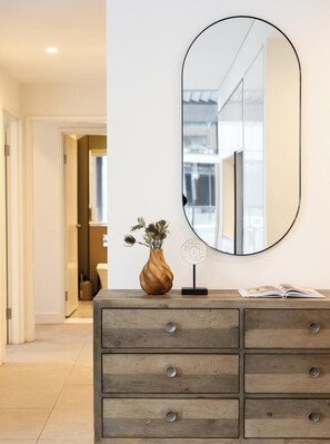 A wooden dresser with a mirror, a vase with dried flowers, and a decorative item. - KozyGuru | Parramatta | Sleek Skyline Retreat (Parramatta)