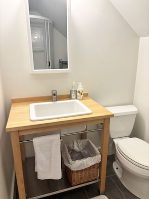 Ein Badezimmer mit einem Holzwaschtisch, einem weißen Waschbecken, einem Spiegel, einer Toilette und einem Mülleimer.