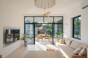 Uma sala de estar moderna com uma televisão grande, um sofá, uma mesa de jantar com cadeiras e um ventilador de teto.