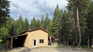 A single-story building with a garage, surrounded by dense forest. - Peaceful Montana Retreat near Glacier National Park (Fortine)
