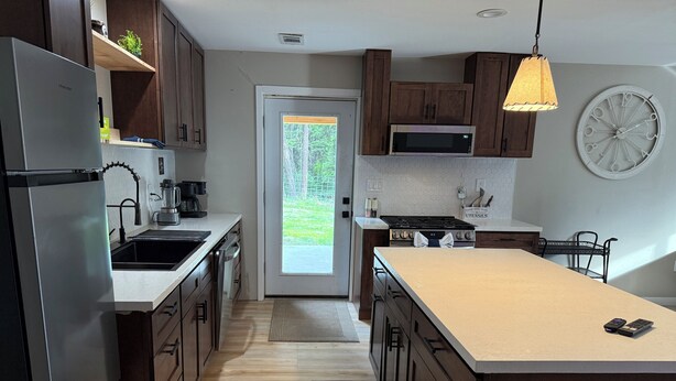 A modern kitchen with a refrigerator, stove, microwave, and wooden cabinets. - Peaceful Montana Retreat near Glacier National Park (Fortine)