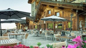 An outdoor dining area with wooden tables and chairs, umbrellas, and potted plants. - Hotel Carlina Belle Plagne (La Plagne-Tarentaise)