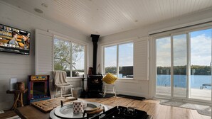 Quarto com mesa de madeira, lareira, televisão e grandes janelas com vista para um corpo de água.